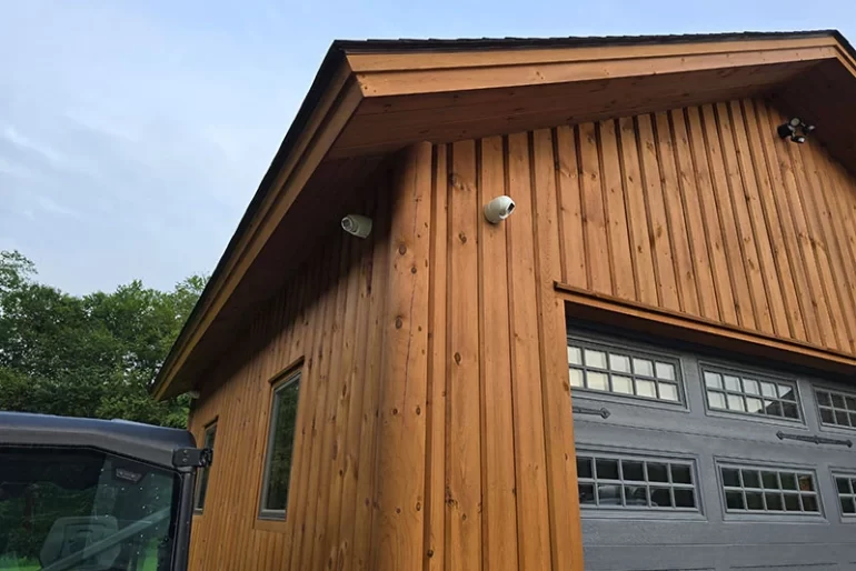 Two turret security cameras mounted high on a wood-sided garage